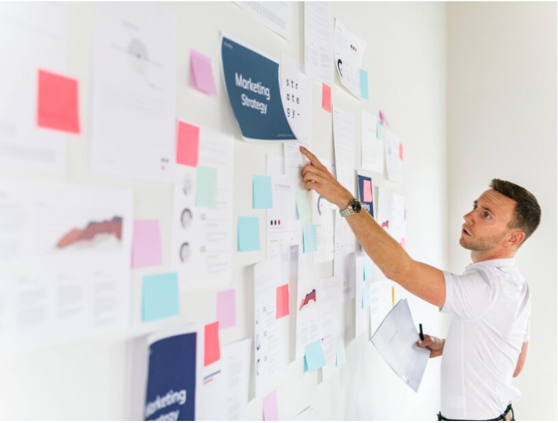 B2B marketing professional analyzing strategy board covered with charts, reports, and sticky notes during a marketing system audit.